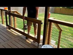 a man standing on top of a wooden deck next to a metal fence and green grass