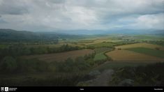 an aerial view of the countryside with trees and hills in the distance under a cloudy sky