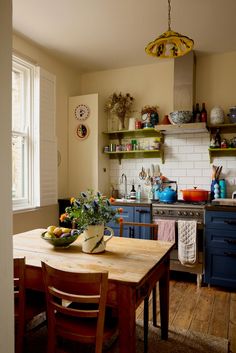 a kitchen with blue cabinets and wooden table in the center, next to an open window