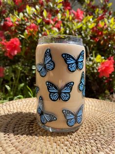 a glass with blue butterflies on it sitting on a table in front of some flowers