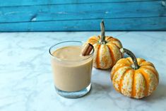 two pumpkins sitting next to a glass of milk on a table with cinnamon sticks sticking out of it