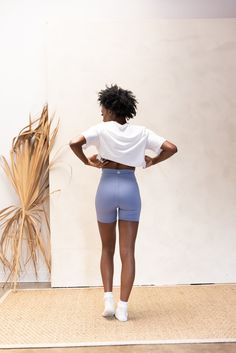 a woman standing in front of a wall with her back to the camera, wearing blue shorts and a white t - shirt