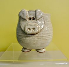 a ceramic piggy bank sitting on top of a clear plastic shelf against a yellow wall