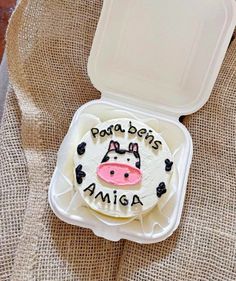 a cake shaped like a cow is in a plastic container on a burlap surface