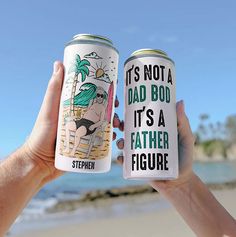 someone holding up two cans of beer on the beach