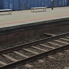 a bench sitting on the side of a train track next to a loading area with blue shipping containers in the background