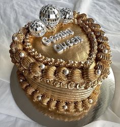 a golden cake decorated with disco balls and the words queen on it's side