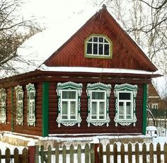 a small wooden house with white windows and green shutters on the front, surrounded by snow