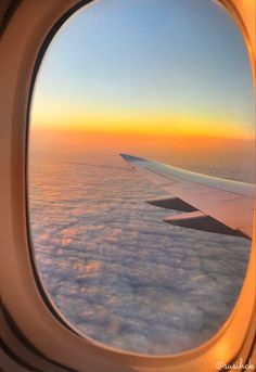 an airplane window with the view of clouds and sunset in the sky from inside it