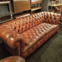 a brown leather couch sitting on top of a carpeted floor next to wooden shelves