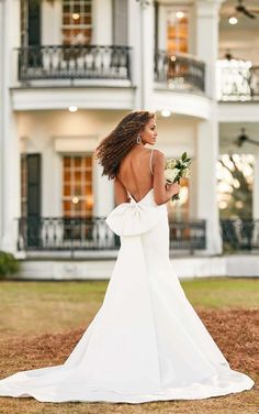 a woman in a white wedding dress is walking towards a large house