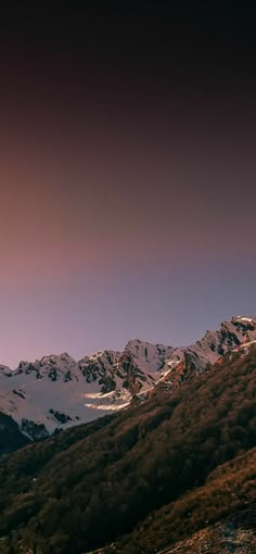 the mountains are covered in snow and brown grass, under a pink - tinged sky