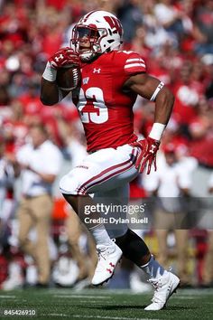 a football player running with the ball in his hand and people watching from the stands behind him