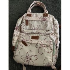 a white flowered backpack sitting on top of a carpet covered floor next to a purse