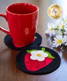 two coasters with flowers on them sitting next to a red coffee cup and white daisies