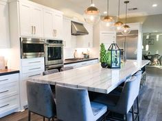 a large kitchen with white cabinets and marble counter tops, stainless steel appliances and pendant lights