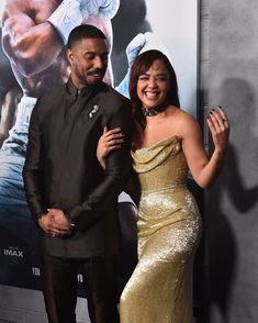 two people standing next to each other on a red carpet in front of a movie poster