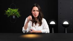 a woman sitting at a table with a potted plant in front of her and lights on the wall behind her