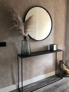 a black console table with a round mirror above it and a vase on the side