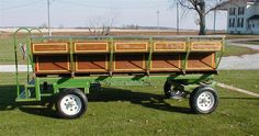 a green wagon with two wooden boxes on it's back and wheels, parked in the grass