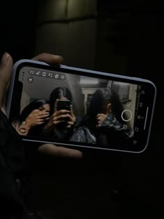 a person holding up a cell phone in the dark with two people taking pictures on it