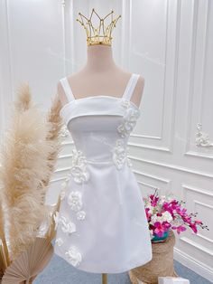 a white wedding dress on display in front of a vase with flowers and a gold crown