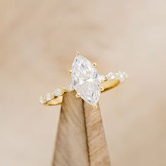 a pear shaped diamond ring on top of a wooden stand with diamonds around the band