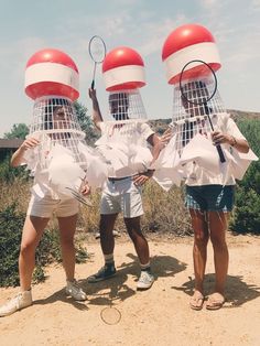 three people wearing identical hats with tennis rackets on their heads in the dirt near bushes