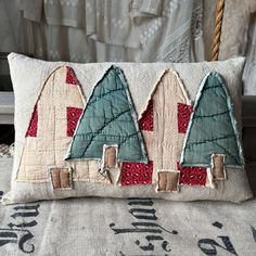 a decorative pillow made to look like houses with trees on the front and sides, sitting on a bed