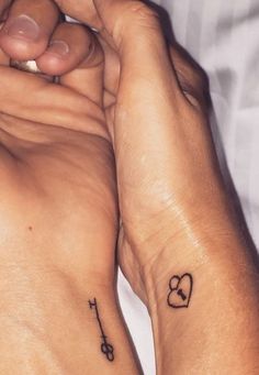 two people holding hands with tattoos on their arms and one has a cross in the middle