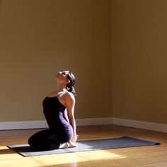 a woman sitting on a yoga mat in the middle of a room with her eyes closed