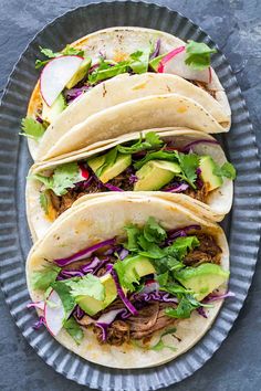 three tacos on a plate with lettuce, cabbage and avocado