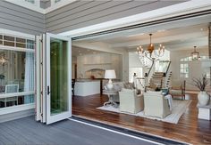 a large open living room and dining room area with wood floors, white furniture and chandelier