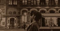 a black and white photo of a man standing in front of a building talking on a cell phone