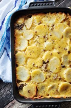 a casserole dish with potatoes and meat in it sitting on a wooden table