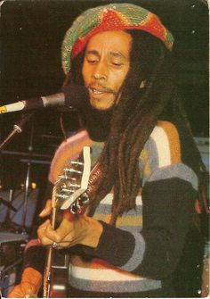 a man with dreadlocks playing a guitar in front of a microphone