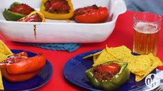 two blue plates topped with stuffed peppers and chips next to a glass of beer on a red table cloth