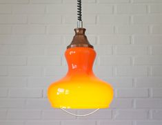 an orange and yellow light hanging from a ceiling fixture in front of a white brick wall