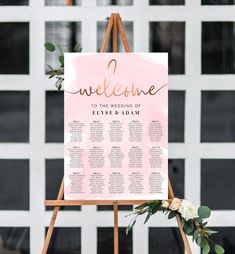 a welcome sign with flowers and greenery on it for an outdoor wedding in front of a white building