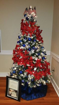 a decorated christmas tree with red, white and blue decorations in a living room next to a framed photo