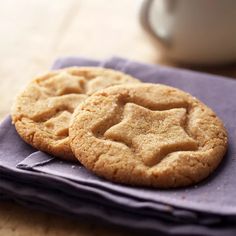 two cookies sitting on top of a purple napkin next to a cup and saucer