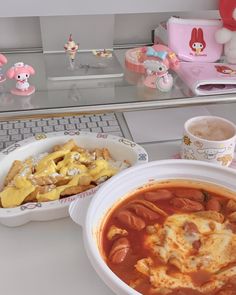 two bowls of food sitting on top of a table next to a laptop computer with hello kitty figurines in the background