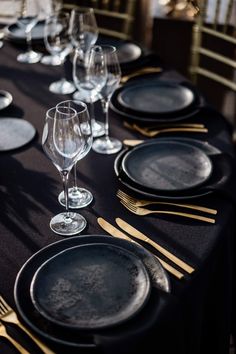 the table is set with black plates and gold cutlery, silverware, and wine glasses