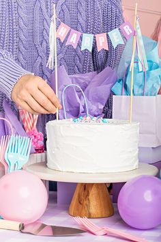 a woman is decorating a birthday cake with pink and blue balloons, streamers and bunting