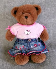 a brown teddy bear wearing a hello kitty shirt and denim skirt with pink bows on it's head