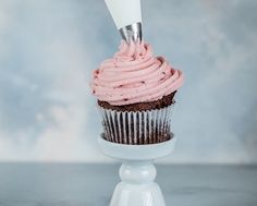 a cupcake with pink frosting on top is being held by a pastry server