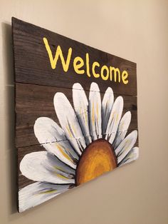 a wooden sign that says welcome with a white flower painted on the front and bottom