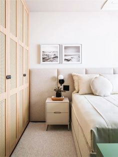 a white bed sitting next to a wooden door in a room with two pictures on the wall