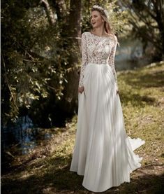 a woman standing in the woods wearing a wedding dress with long sleeves and sheer lace