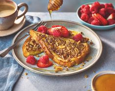 french toast with strawberries and honey being drizzled over it on a plate